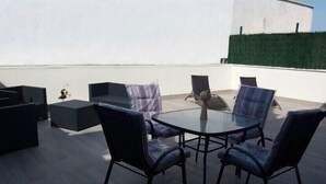 A rooftop terrace with a glass table surrounded by chairs, a sofa, and a small table.