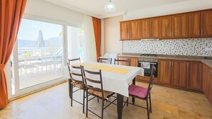 Ein Essbereich mit einem Tisch für vier Personen, Holzausbau, einer gefliesten Spritzschutzleiste und Blick auf Pool und Berge durch große Fenster.