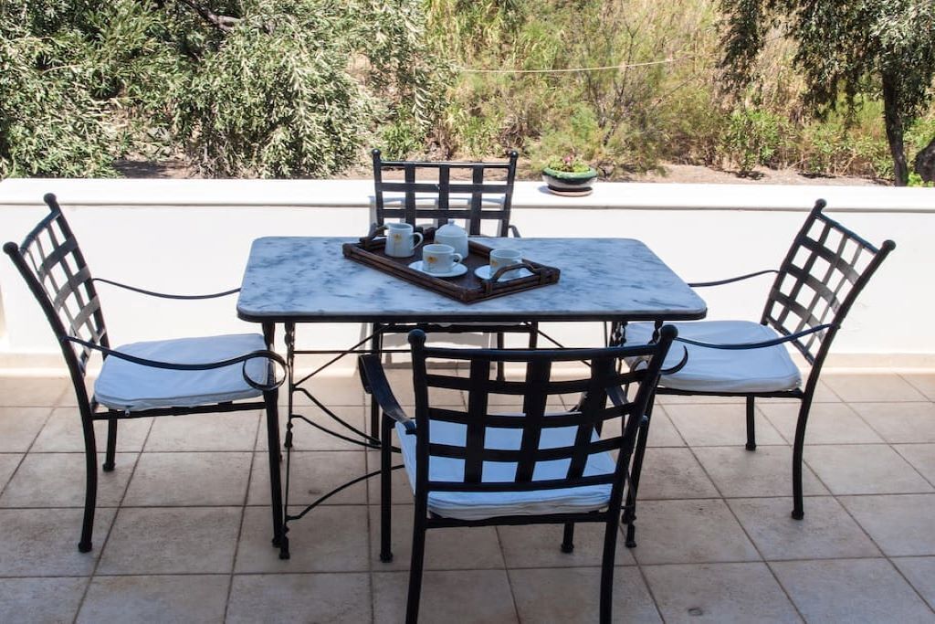 Eine Terrasse mit Tisch und vier Stühlen, ein Tablett mit Tassen und einem Teekessel, und im Hintergrund ein Blumentopf.