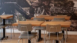 A restaurant with wooden tables and chairs, a mural of a man in a hat, and a mountainous background. - Fisherman Hótel Suðureyri (Sudureyri)