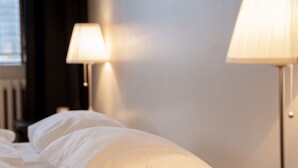 A neatly made bed with white linens, a small decorative item on the nightstand, and two table lamps. - Fisherman Hótel Suðureyri (Sudureyri)