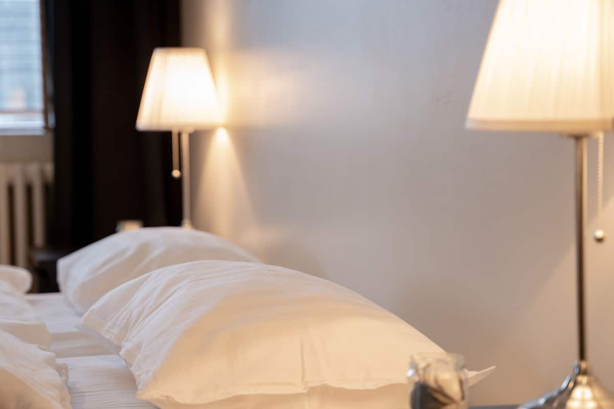 Ein ordentlich bezogenes Bett mit weißen Laken, ein kleines dekoratives Objekt auf dem Nachttisch und zwei Nachttischlampen.