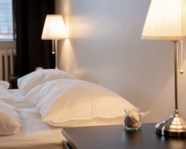 Una cama bien tendida con sábanas blancas, un pequeño objeto decorativo en la mesita de noche y dos lámparas de mesa.