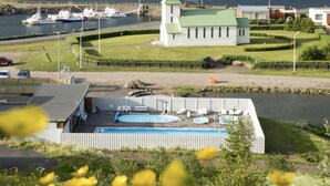 A church with a green roof and a white fence in front of a body of water. - Fisherman Hótel Suðureyri (Sudureyri)
