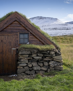 Una cabaña de madera con base de pared de piedra, una puerta y un ventanal.