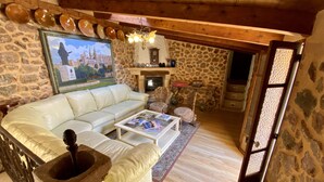 Una sala de estar acogedora con pared de piedra, chimenea, sofá de cuero blanco y una mesa de centro con revistas.