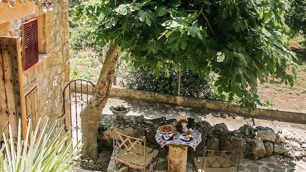 Un patio al aire libre con suelo de piedra, una mesa cubierta con mantel, sillas y un frutero.