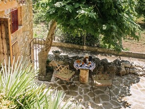 Un patio al aire libre con suelo de piedra, una mesa cubierta con mantel, sillas y un frutero.