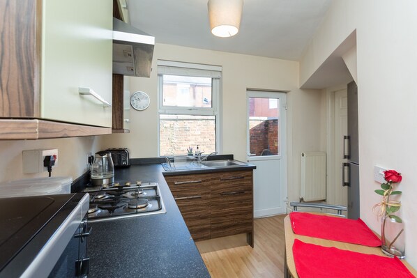 A compact kitchen with a gas stove, a coffee maker, and a sink. There is a window with a view of a brick building outside.