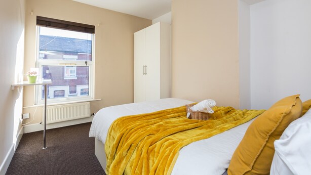 Een slaapkamer met een bed, een raam, een radiator en een kledingkast.