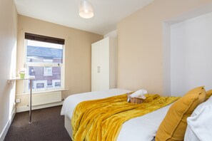 A bedroom with a bed, a window, a radiator, and a wardrobe.
