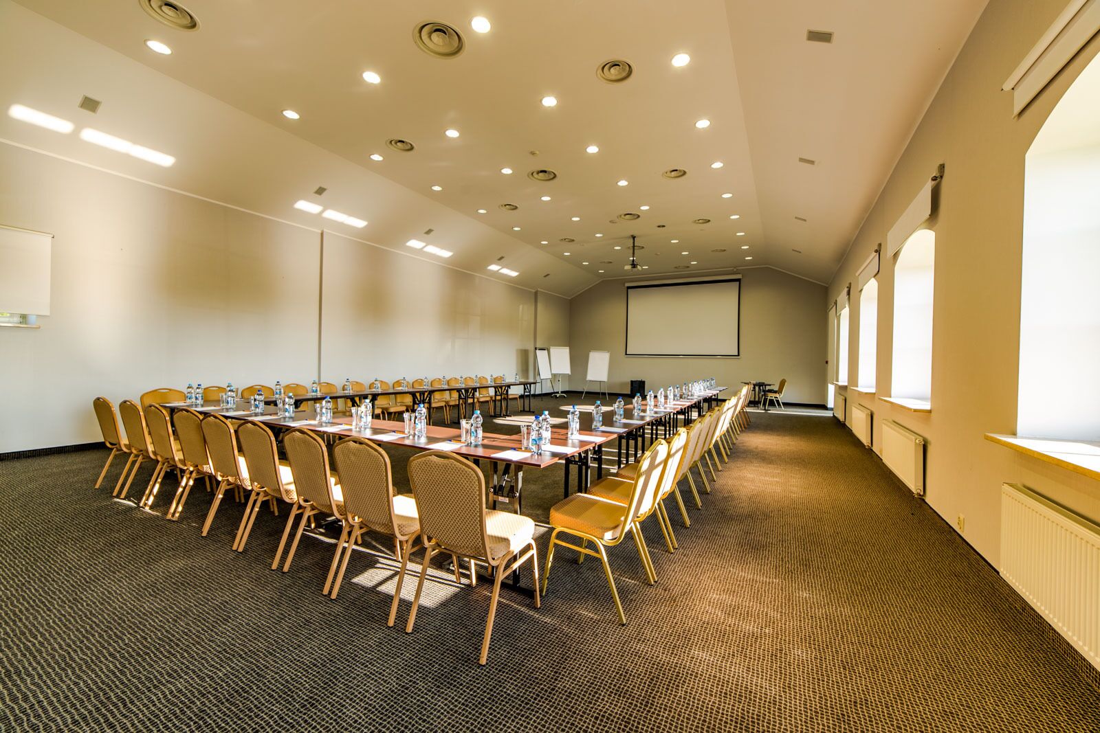 Ein Konferenzraum mit langem Tisch, Stühlen, einer Projektionsleinwand und Teppichboden.