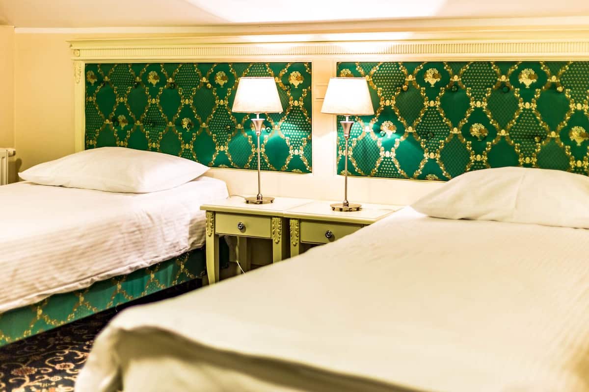 Quarto de hotel com duas camas de solteiro, pequenas mesas de cabeceira com luminárias e cabeceira estampada verde.