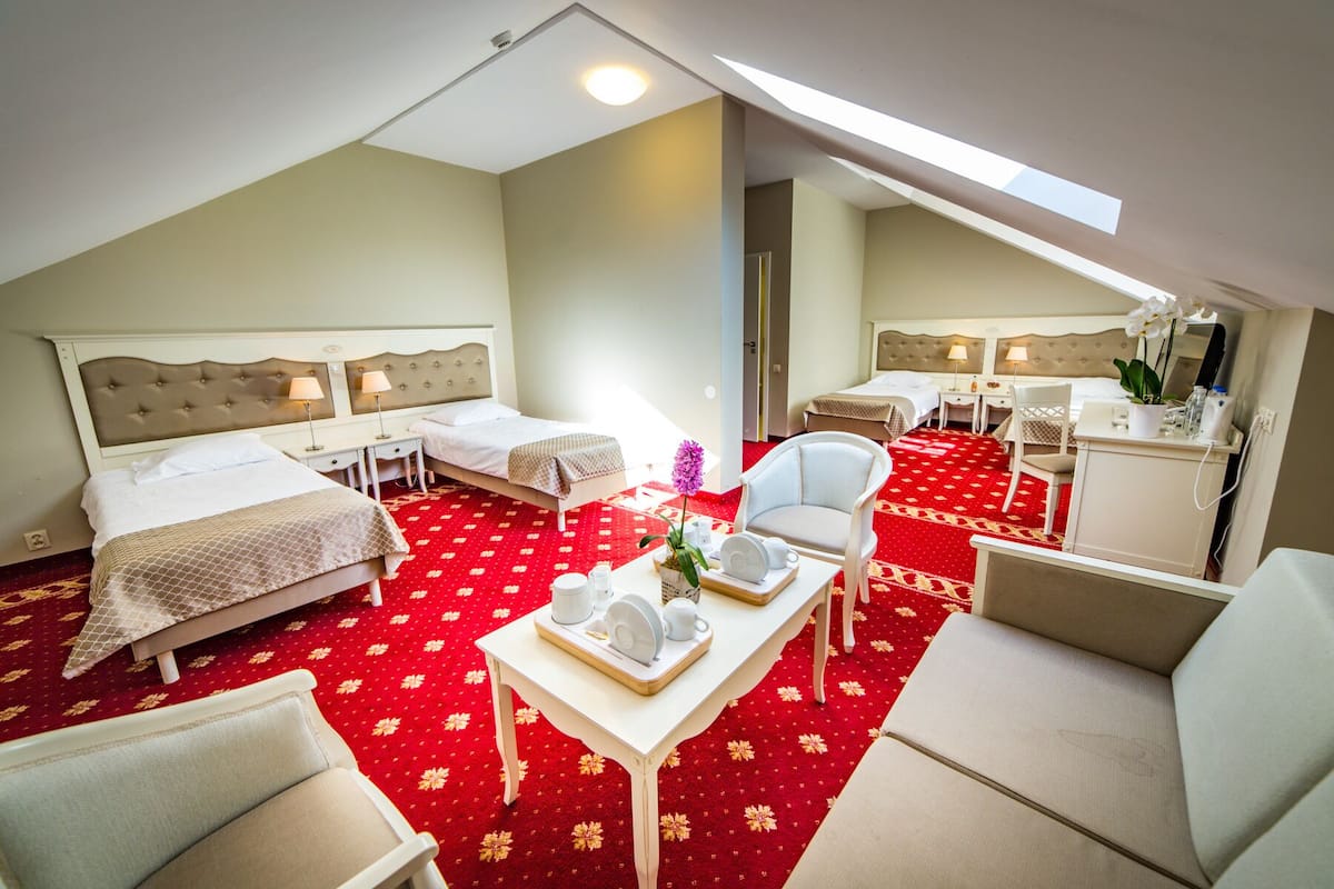Quarto de hotel com duas camas, uma escrivaninha, uma cadeira e uma mesinha de centro com um vaso de flores.