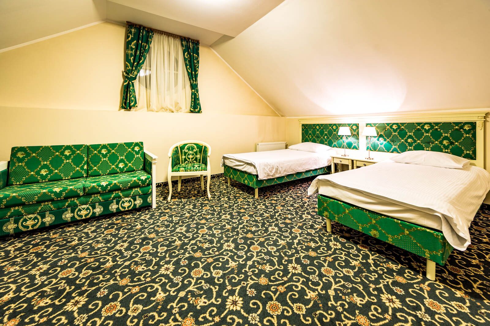 Een hotelkamer met twee eenpersoonsbedden, een groene bank, een stoel en een kleine tafel.