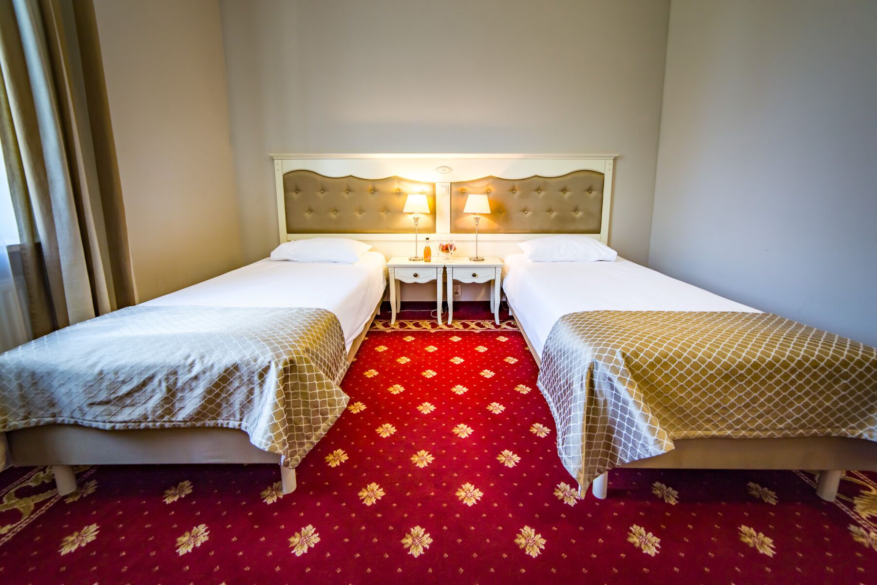 A hotel room with two beds, a red floral carpet, and a white headboard.