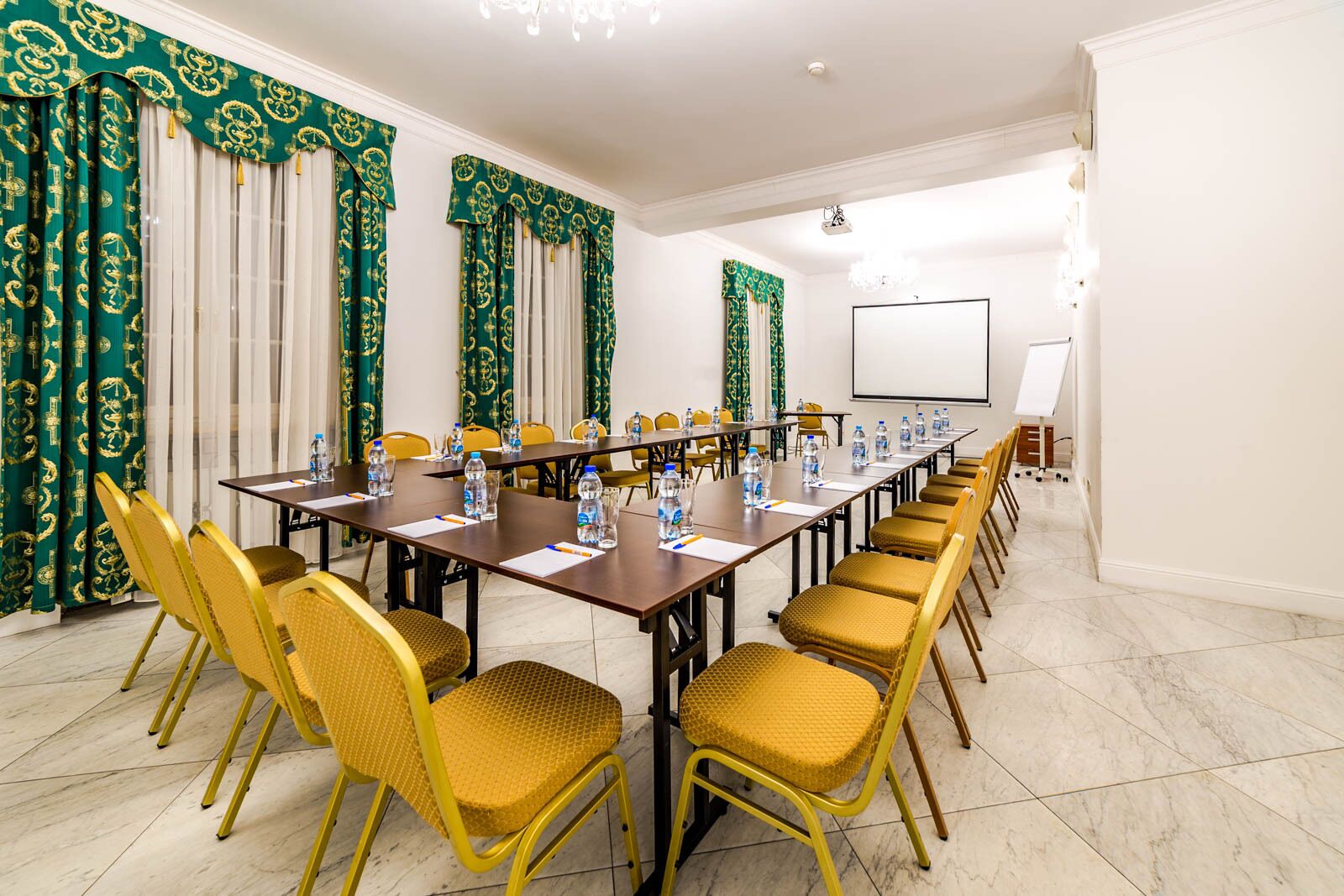 Una sala conferenze con un lungo tavolo, sedie gialle e tende a motivi verdi.