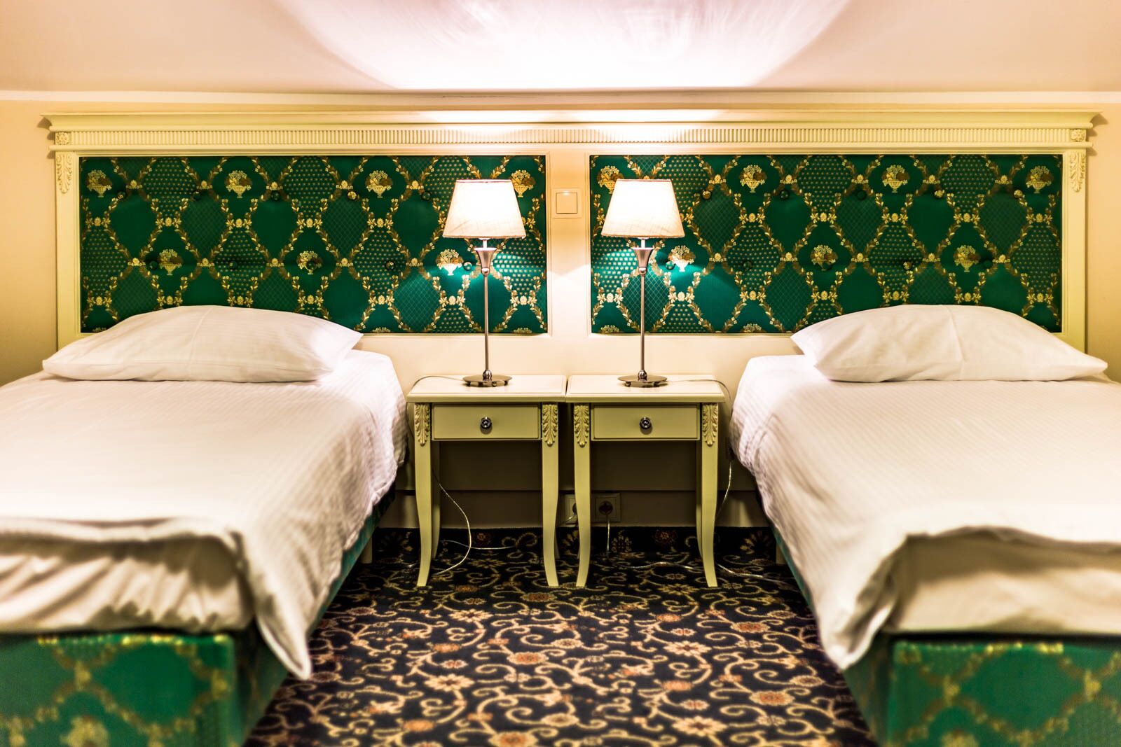 A hotel room with two single beds, a green patterned headboard, and a matching green carpet.