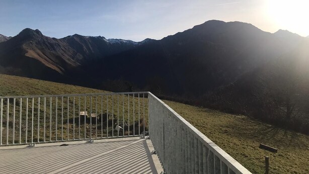 Une plateforme d’observation en béton, dotée d’une rambarde métallique, qui offre une vue panoramique sur un paysage montagneux.