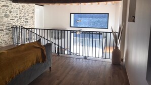 Une pièce de style « loft » avec un mur en pierre, un plafond en bois, un balcon doté d’une rambarde en métal et une grande fenêtre.