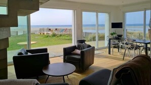 Ein modernes Wohnzimmer mit einem großen Schiebeglasfenster, das auf einen Balkon mit Blick auf den Strand führt.