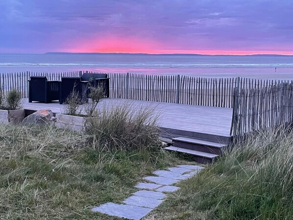 Une terrasse en bois offrant une vue sur l’océan au coucher du soleil.