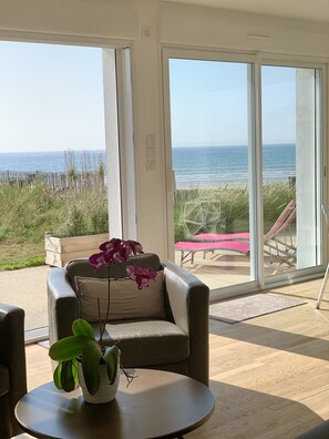 Ein Zimmer mit Blick auf den Strand, ein Sessel, ein Tisch mit einer Pflanze und eine Bank draußen.