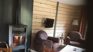 A cozy room with a wood-burning stove, a television mounted on the wall, and two leather chairs. - the shepherd's chalet. (Ventron)
