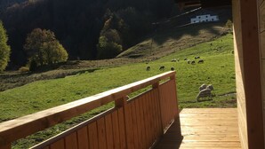 A wooden deck with a view of a green field and a white building in the distance. - the shepherd's chalet. (Ventron)