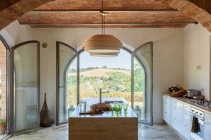Una cocina con una isla central, una lámpara colgante y amplios ventanales de arco que dan vistas al campo.