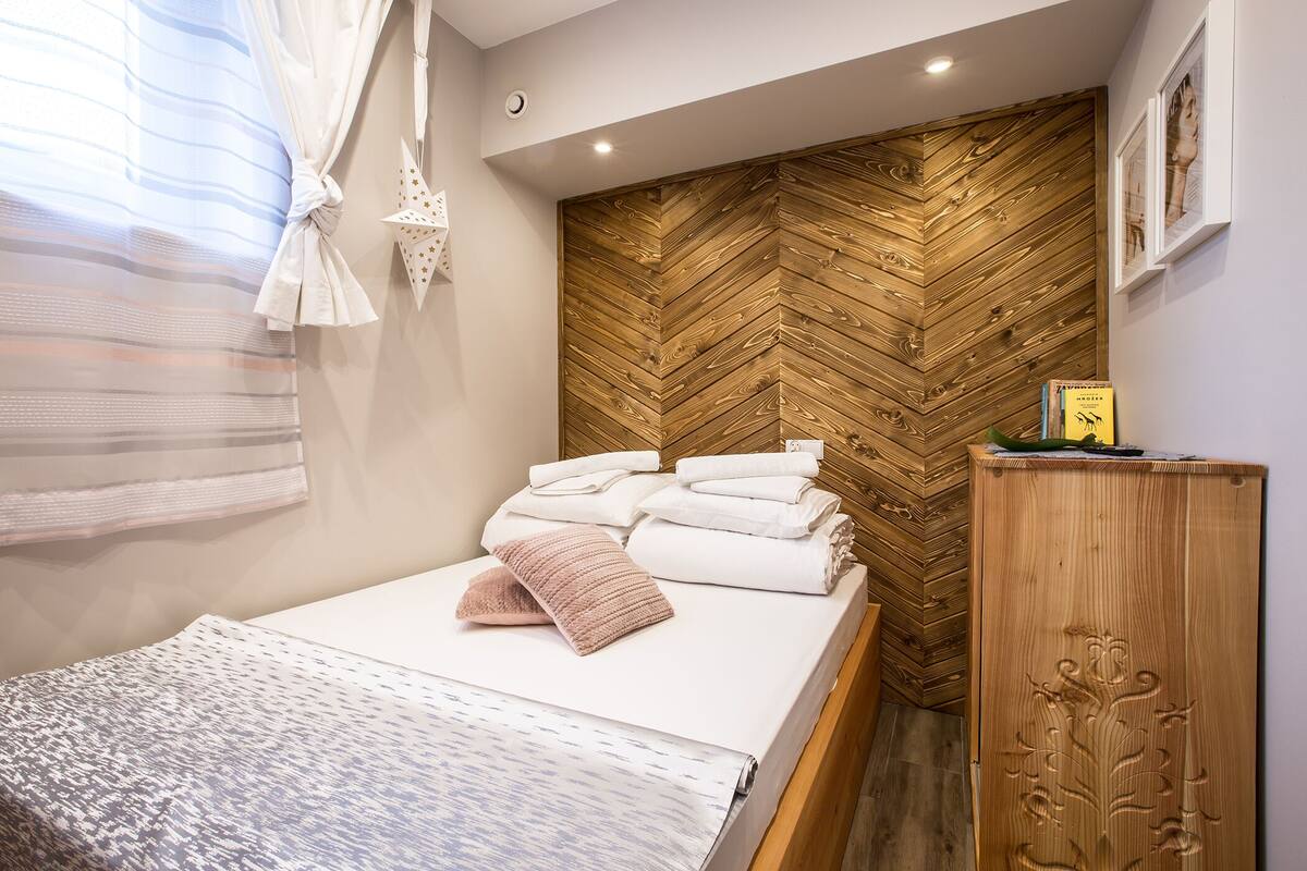 A neatly made bed with folded towels, a wooden headboard, and a small cabinet with a decorative design.