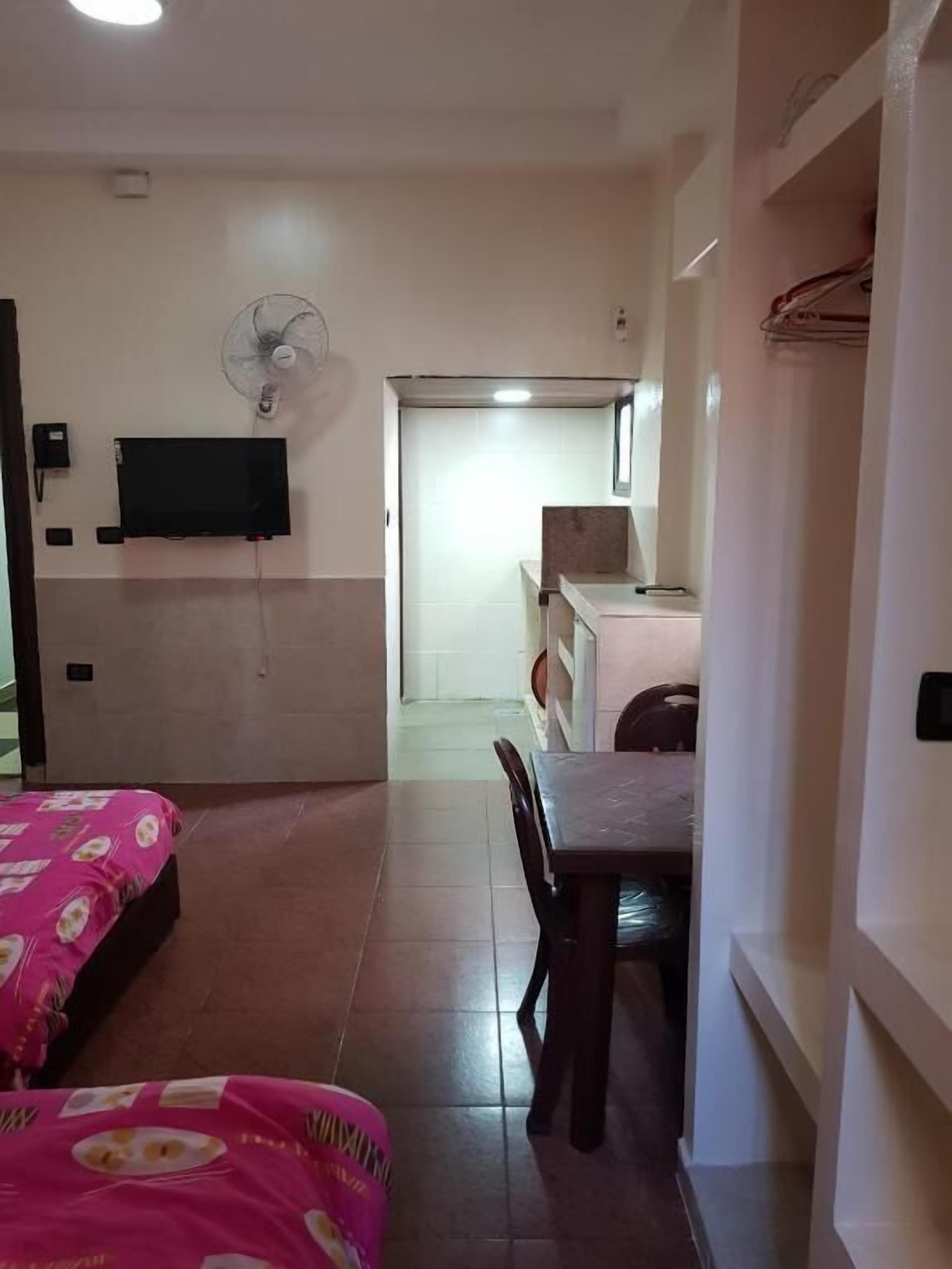 A hotel room with a bed, a desk, a chair, a television, and a fan.