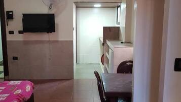 A hotel room with a bed, a desk, a chair, a television, and a fan.