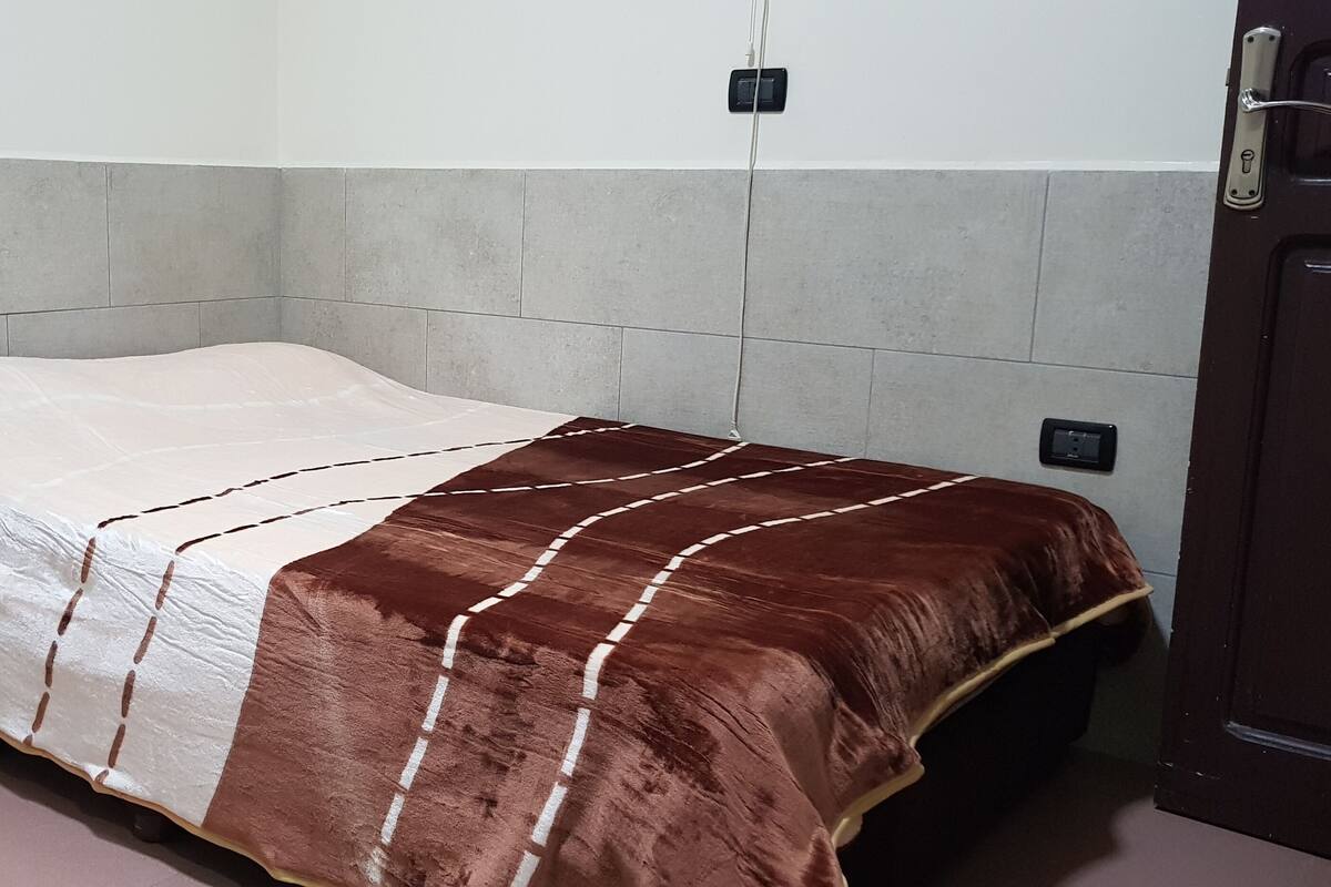 A small, single-bed room with a plain bedspread and a door to the right.