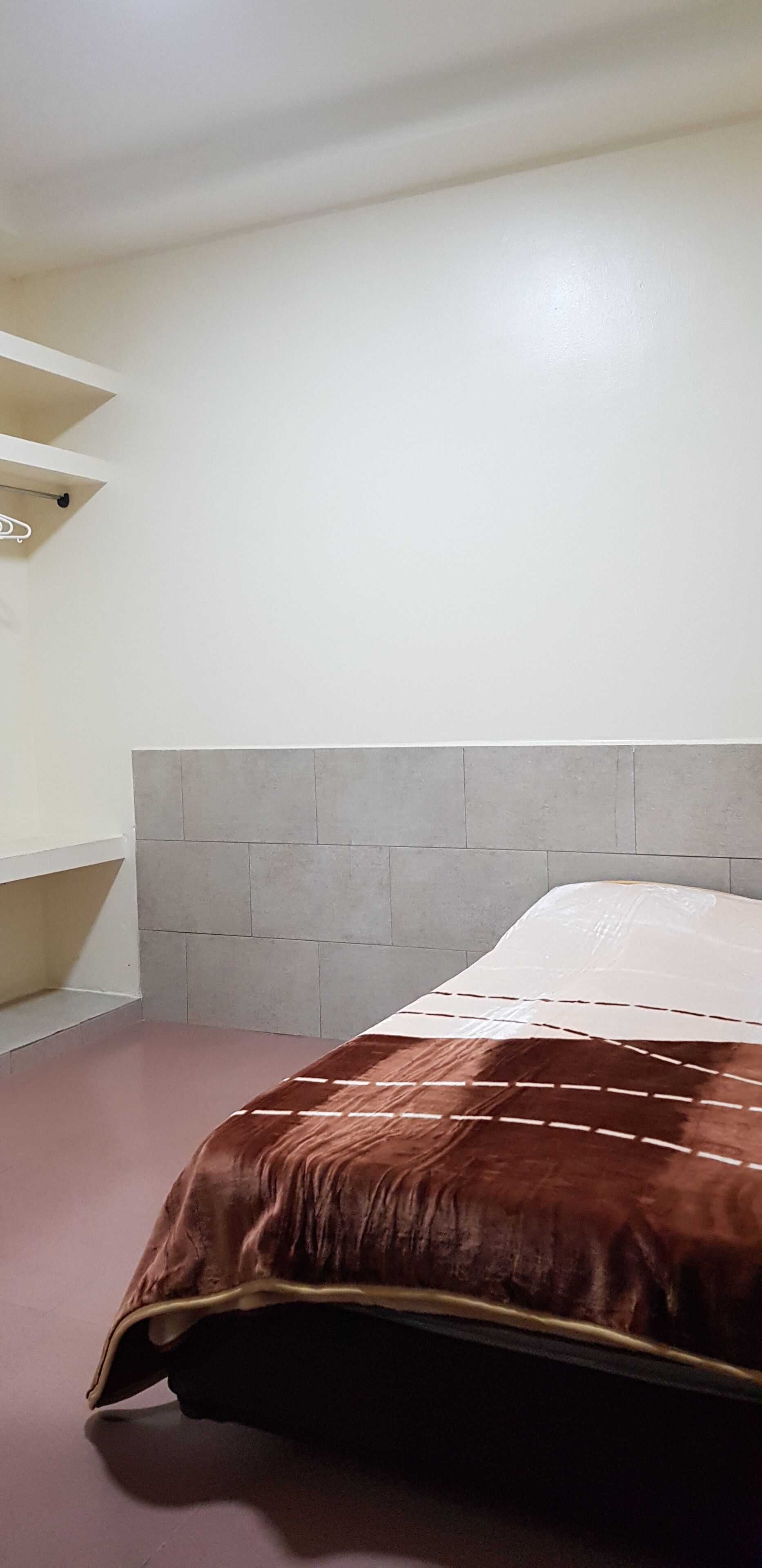 A bedroom with a bed, a headboard, a shelf, and a wall.