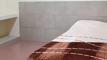 Un dormitorio con cama, cabecera, estante y pared.