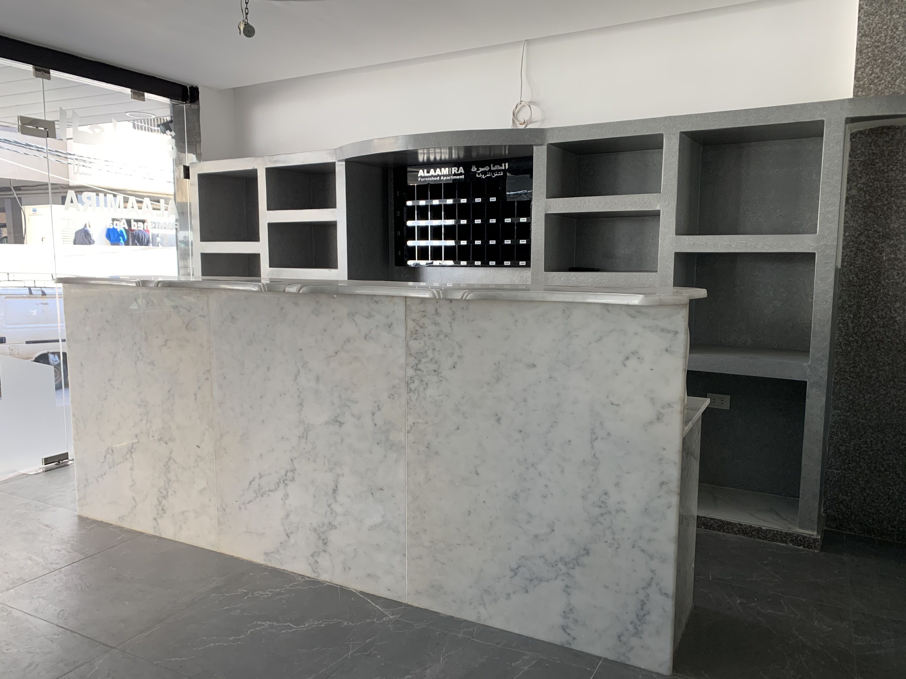 Un comptoir d’accueil avec un plateau en marbre et des étagères noires.
