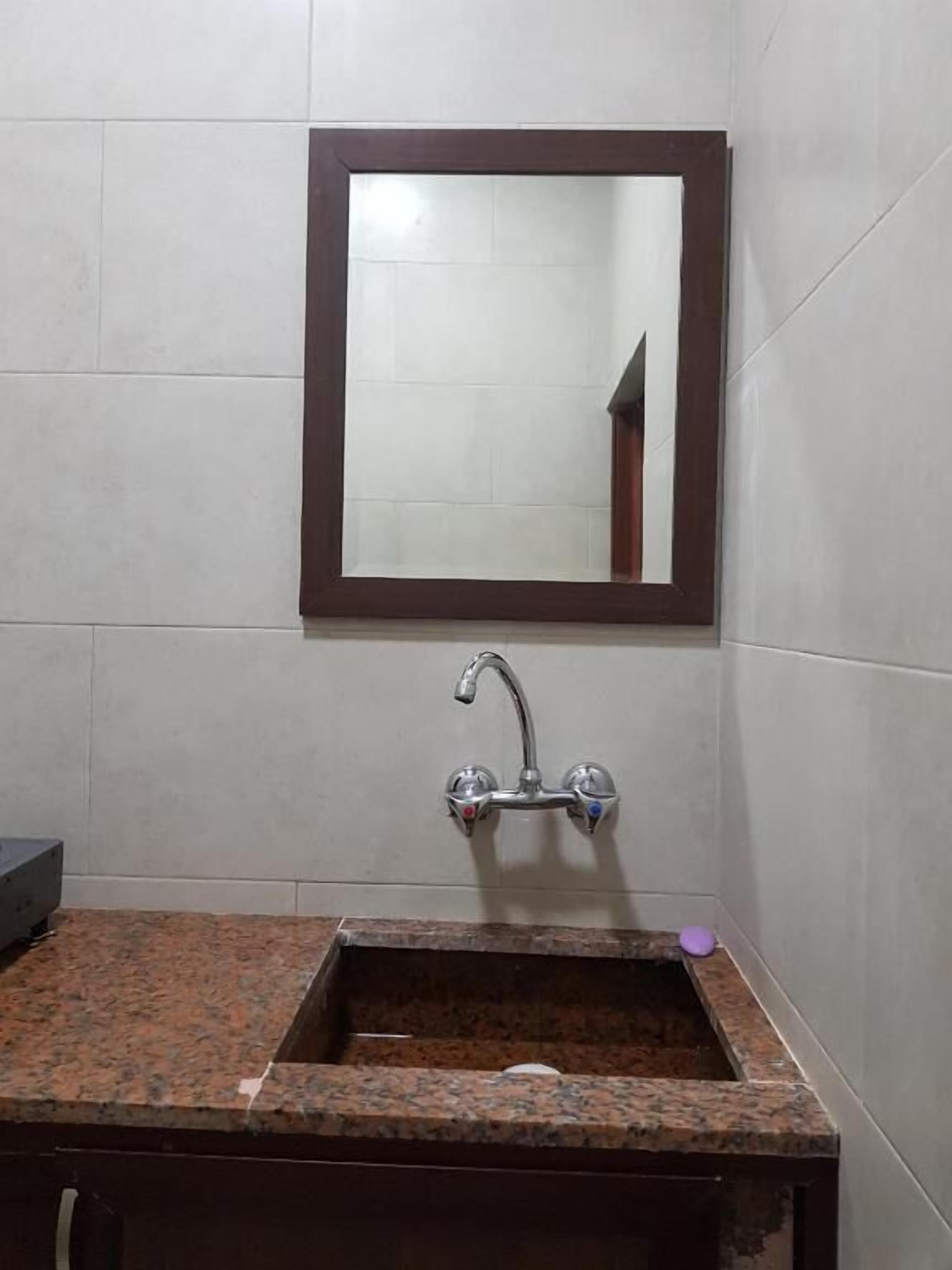 A bathroom with a granite sink, a mirror with a wooden frame, and a faucet.