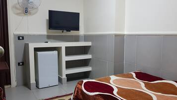 A small, clean room with a bed, a TV mounted on the wall, a small fridge, and a heater.
