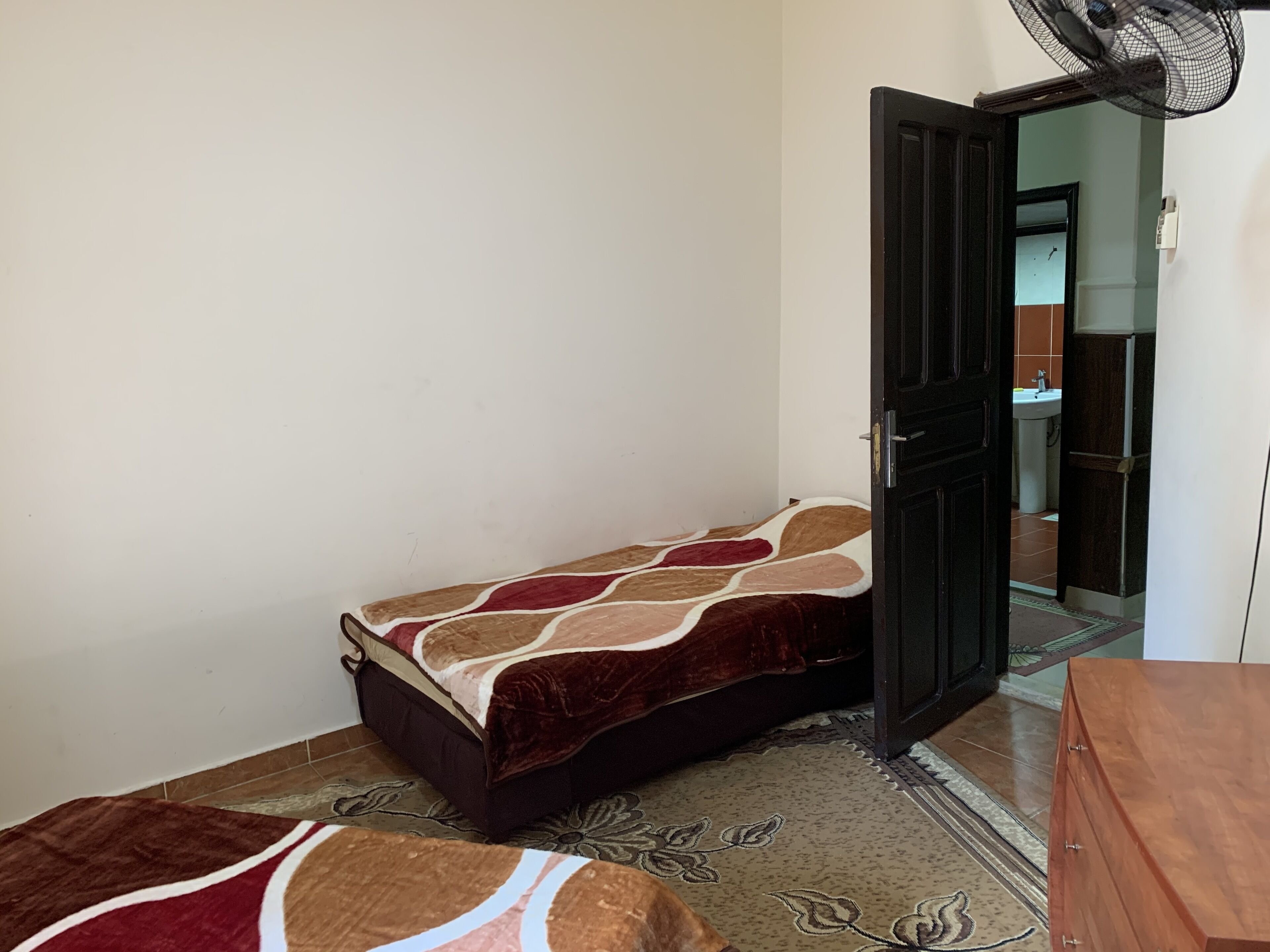 Una habitación pequeña con cama individual, una colcha estampada, un armario de madera y suelo de baldosas.