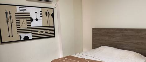 A bedroom with a bed, a headboard, a wall-mounted air conditioner, and a patterned rug.