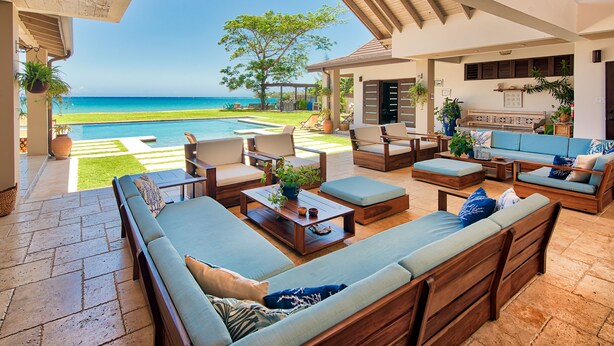 A spacious living area with a view of the ocean, a pool, and outdoor furniture.