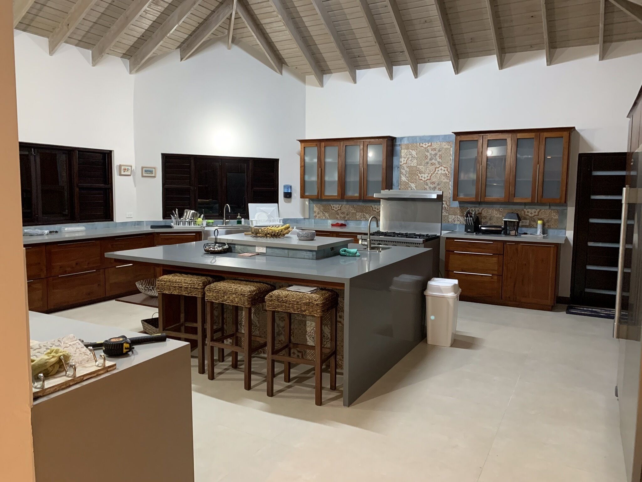 A modern kitchen with a large island, wooden cabinets, and a high ceiling.