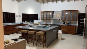 A modern kitchen with a large island, wooden cabinets, and a high ceiling.