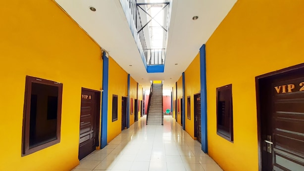 Un pasillo largo e iluminado, con paredes amarillas y detalles azules, que conduce a una escalera.