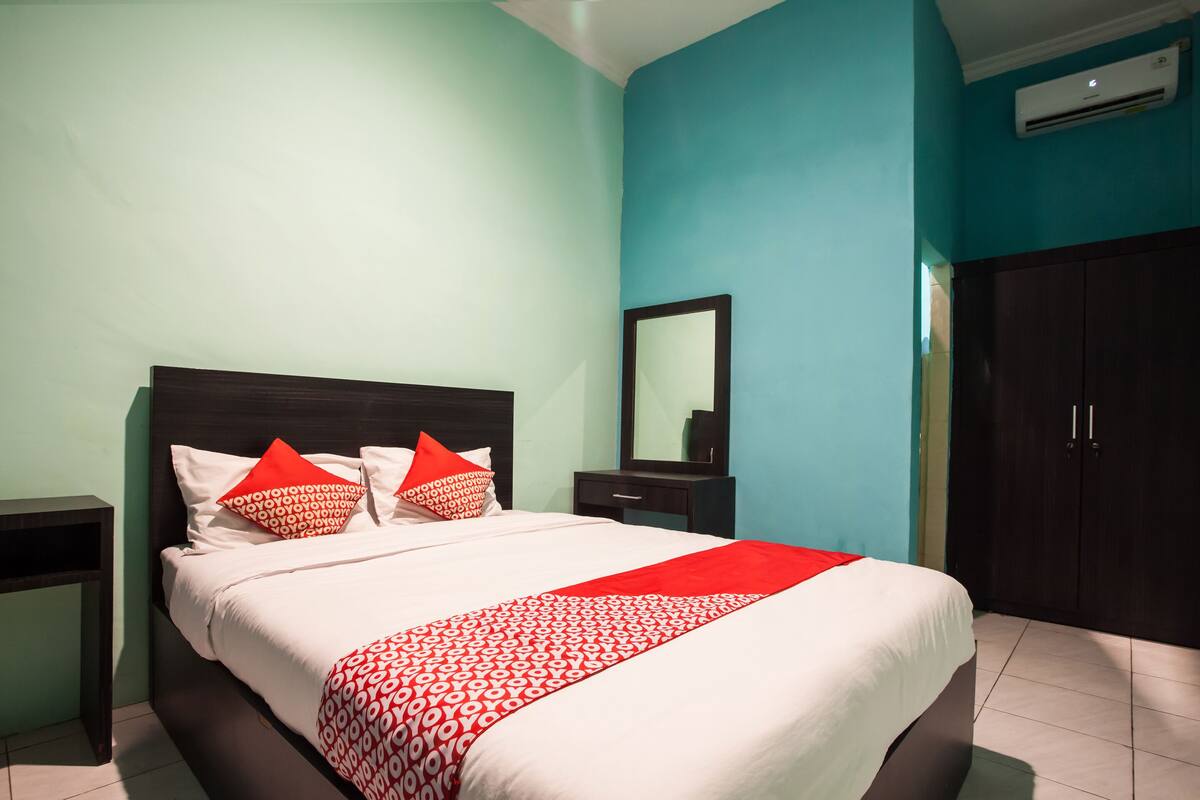 A neatly made bed with a patterned bedspread, a nightstand, a dresser, and a wardrobe in a room with teal walls and a white ceiling.