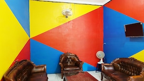 Una habitación con un diseño geométrico en la pared, un sofá de cuero marrón, un sillón a juego, una mesita y un televisor montado en la pared.