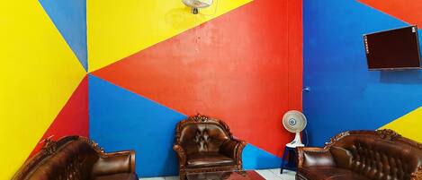 A room with a geometric wall design, a brown leather sofa, a matching armchair, a small table, and a wall-mounted TV.