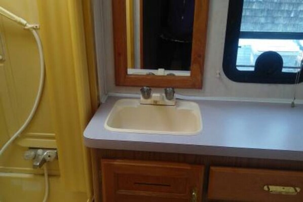 A compact bathroom with a sink, mirror, and wooden cabinetry. - RV suite near El Cerrito BART (El Cerrito)