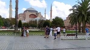 A public square with a mosque, palm trees, and people.